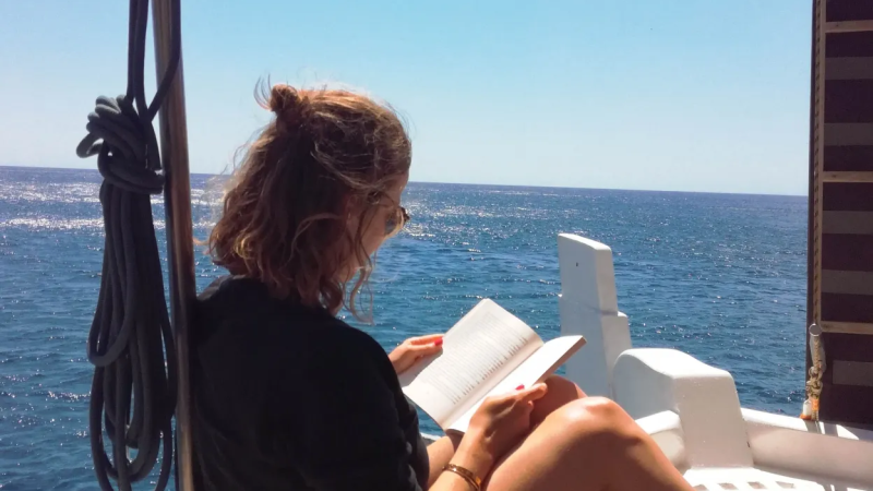 Person sitting on boat deck reading a book with ocean view.