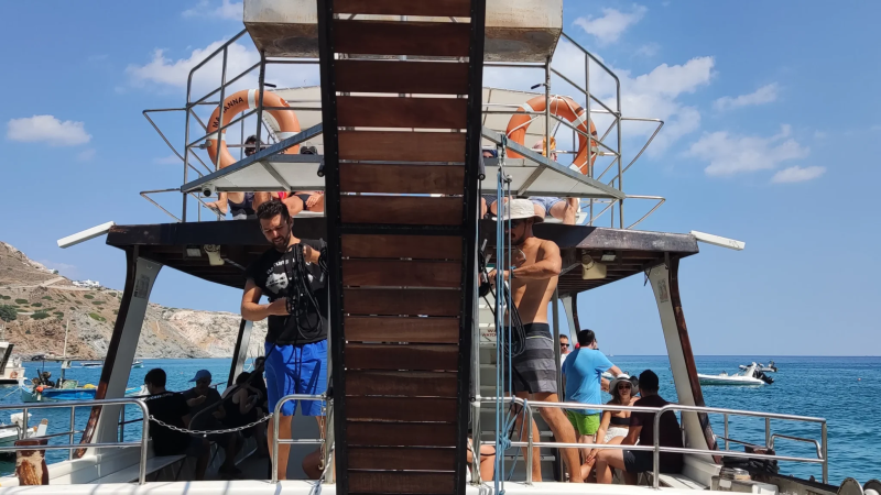 People on a boat preparing for diving, with clear blue sea and other boats in the background.